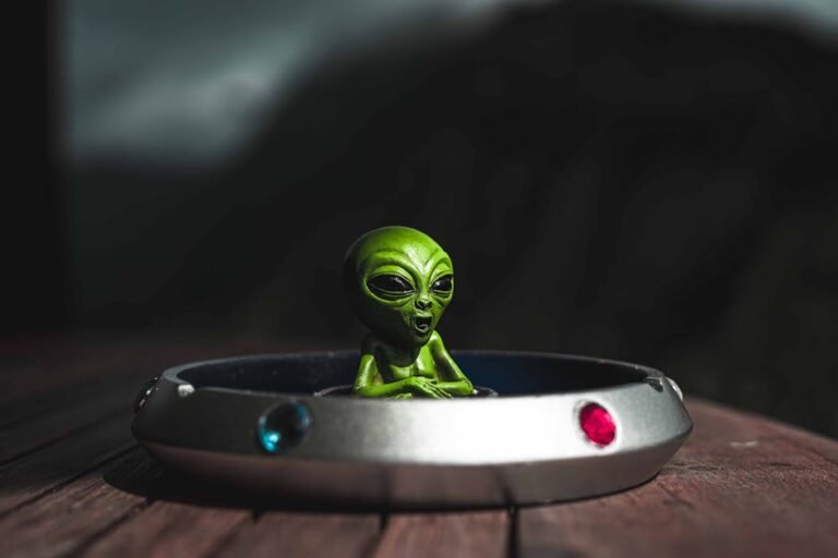 Green alien toy sitting in a spaceship-themed ashtray, outdoors with dramatic lighting.