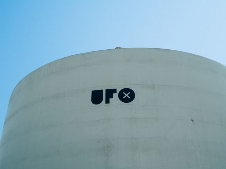Minimalist image of a white cylindrical structure with 'UFO' text under a clear blue sky.