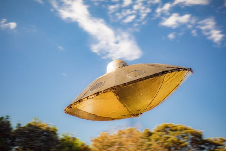 Close-up of a metallic UFO model flying against a clear blue sky background.