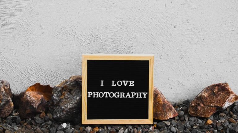 Black letter board with 'I Love Photography' text against rocks and white wall.
