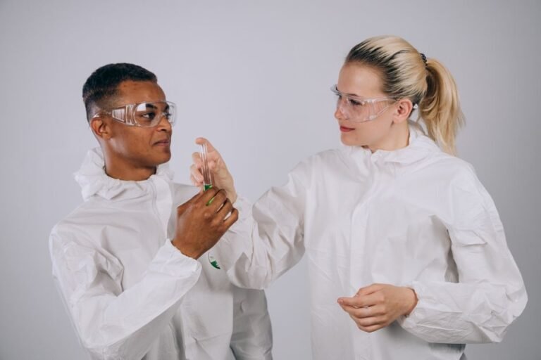 Two scientists in protective gear working together with a test tube in a laboratory setting.