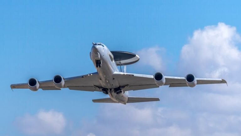 A military AWACS aircraft captured mid-flight against a bright clear sky over Albacete, Spain.