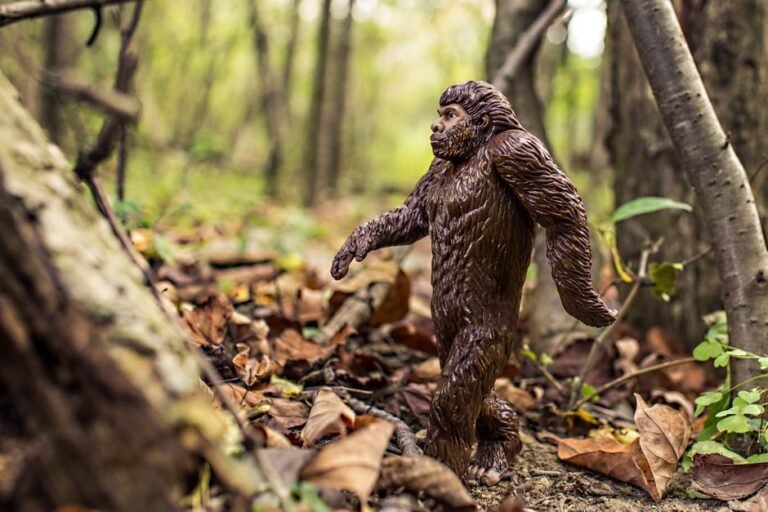 A detailed Bigfoot toy model walking through a forest with fallen leaves, creating a natural wilderness scene.