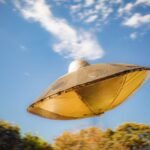 Close-up of a metallic UFO model flying against a clear blue sky background.