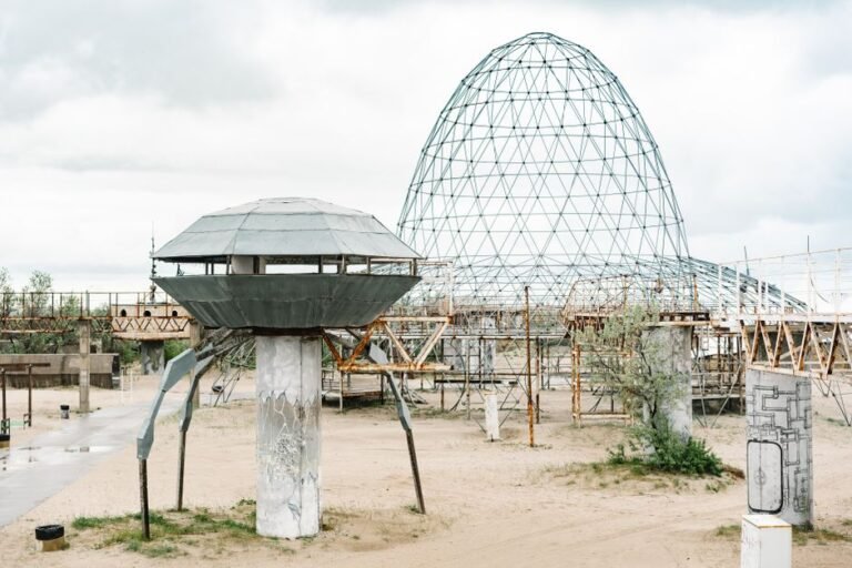 A metallic UFO-like structure in a deserted, sandy park under cloudy skies.