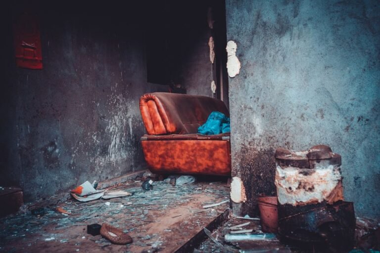 A decaying interior featuring an old leather sofa with debris scattered on the floor.