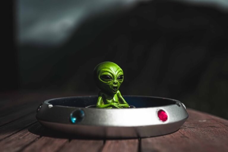 Green alien toy sitting in a spaceship-themed ashtray, outdoors with dramatic lighting.