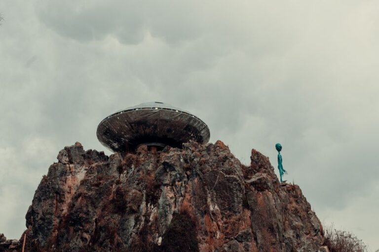 A surreal scene with a UFO and alien standing atop a rugged rock formation against a cloudy sky.