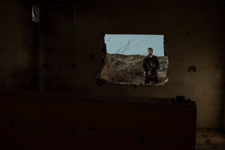 A man stands outside a rough hole in a dark, abandoned building.