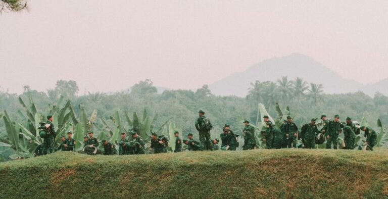 A group of soldiers in green uniforms march through lush jungle terrain, showcasing military training.