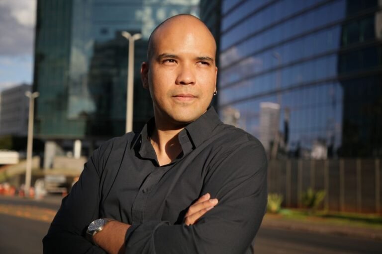 Portrait of a confident man outdoors against a modern glass building in bright daylight.